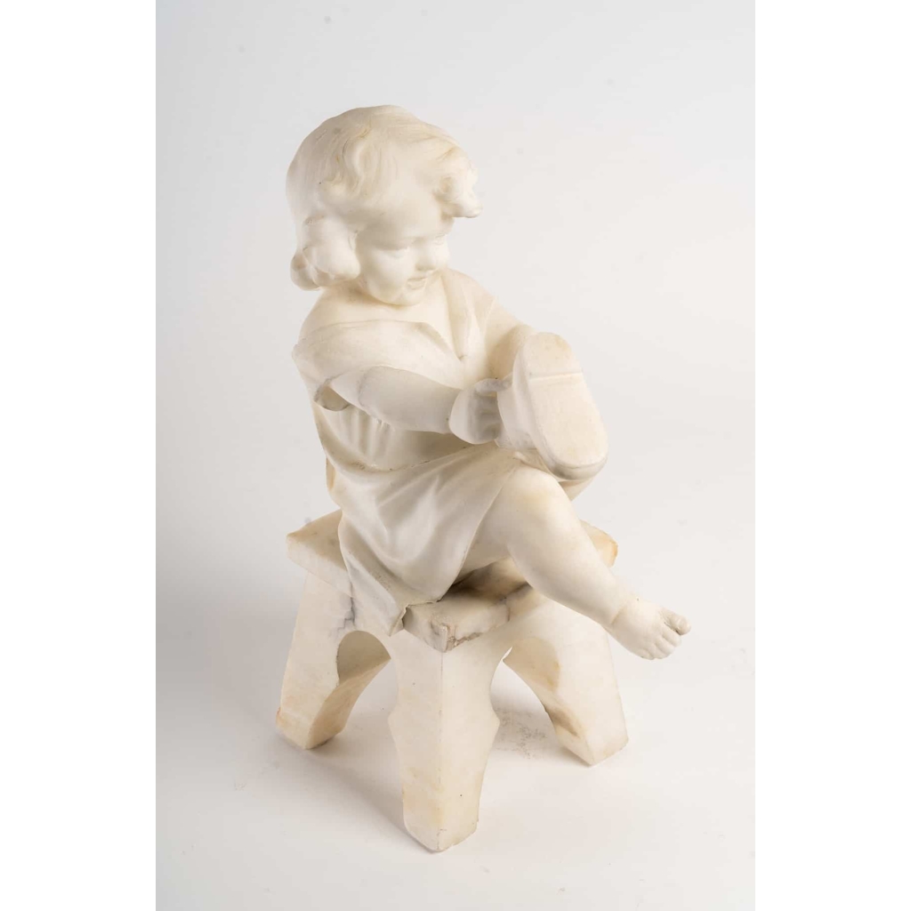 Statue en albâtre représentant une petite fille assise sur un tabouret et jouant avec des chaussures . Statue en albâtre représentant une petite fille assise sur un tabouret et jouant avec des chaussures .