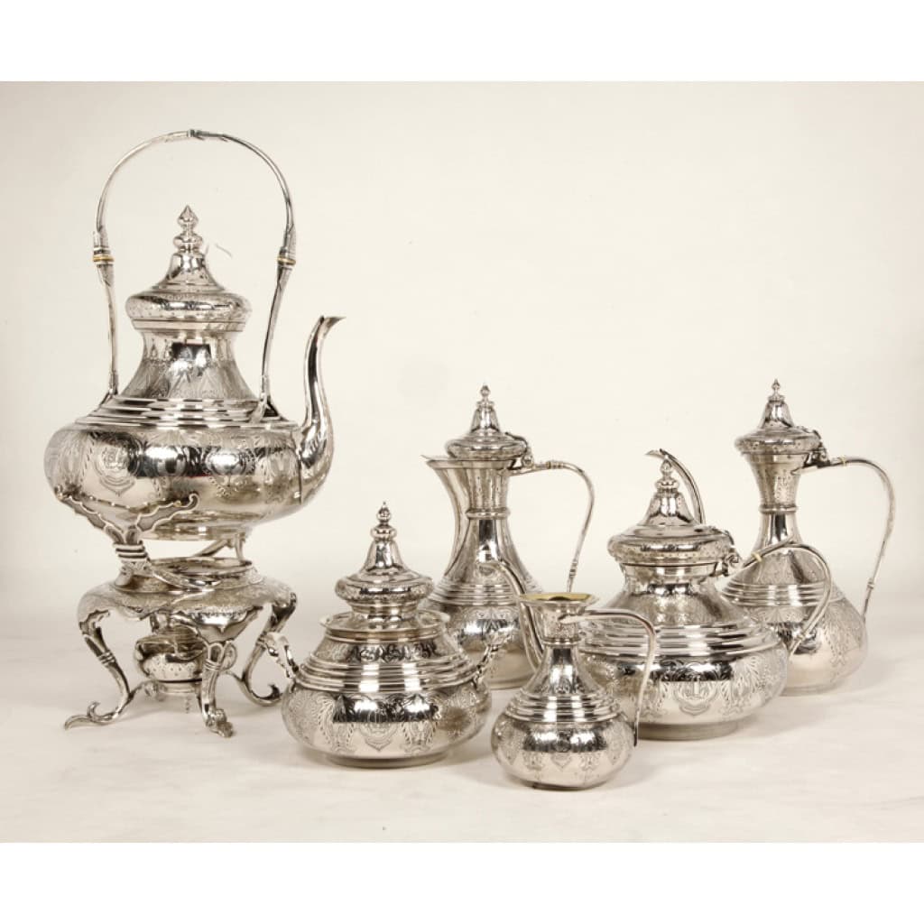 Orfèvre Duponchel - Service thé café en argent massif style Ottoman XIXe Orfèvre Duponchel - Service thé café en argent massif style Ottoman XIXe Service thé / café en argent massif dans le goût ottoman comprenant une cafetière, une théière, un crémier et un sucrier couvert , une verseuse à eau chaude en argent et son samovar et son brûleur sur un trépiéd en métal argenté. Chaque pièce est entièrement gravée à l'acide de motifs orientaux sur fond amati, le corps est ceinturé de quatre filets. L'intérieur du sucrier et du pot à lait est légèrement vermeillé. Dimensions SAMOVAR : hauteur 45 cm - Cafetière: hauteur 26 cm Matières : Argent massif ( 5 pièces) et métal argenté pour le samovar. Poinçon : Minerve 1er titre Epoque : vers 1865 Ces cinq pièces portent le monogramme "L L" provenance FAMILLE LAZARD.